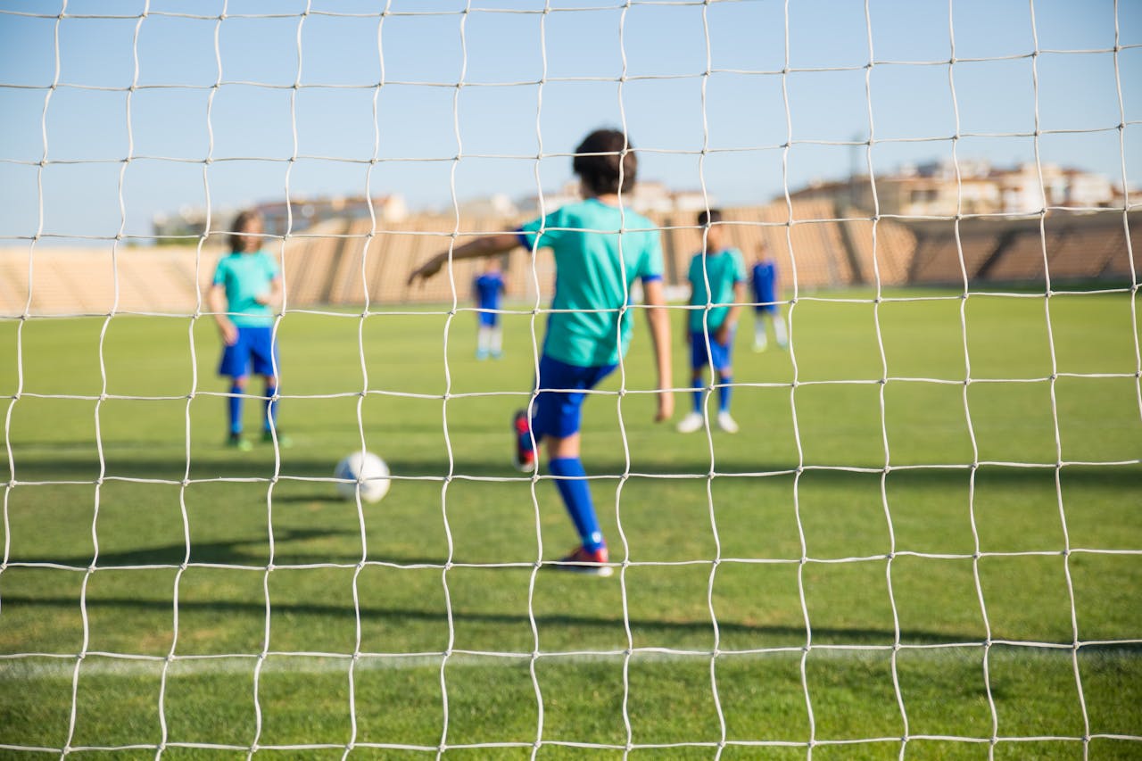 Group of children playing soccer on a sunny day in Portugal, seen through the goal net.